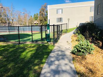 A walkway leads to a building with a tennis court behind a fence.